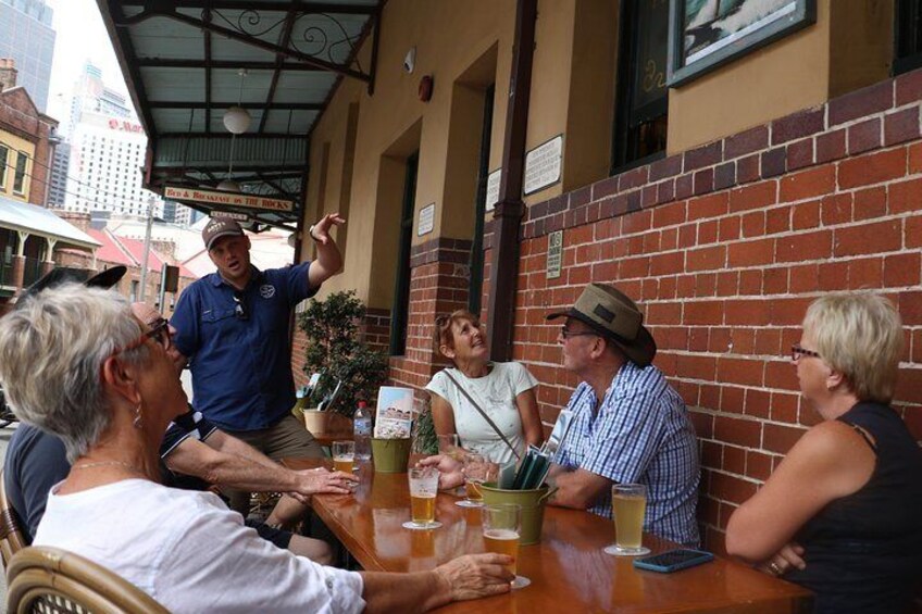 A group of people sitting at an outdoor table in a cafe with brick walls and a metal roof. 2