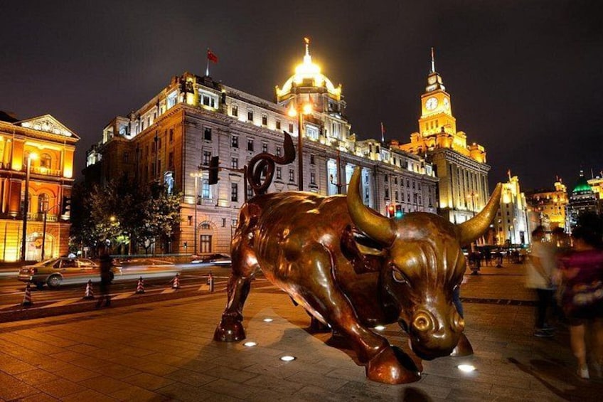 A large bronze bull statue in a public square with illuminated buildings in the background. 2