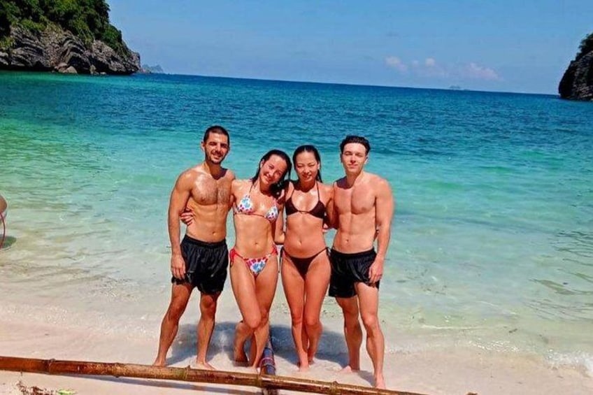 Un grupo de personas de pie en una playa con agua turquesa cristalina y un promontorio rocoso al fondo. 5