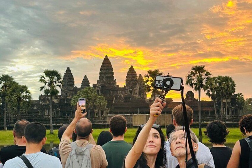 A group of people taking photos of a temple with a sunset in the background. 3