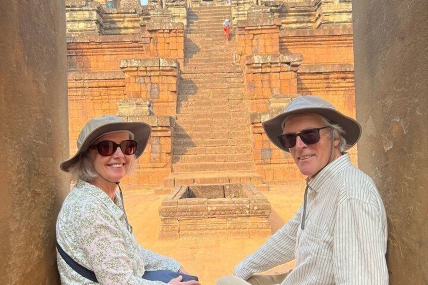 Two people standing in front of an ancient stone structure with steps leading up to a platform. 2