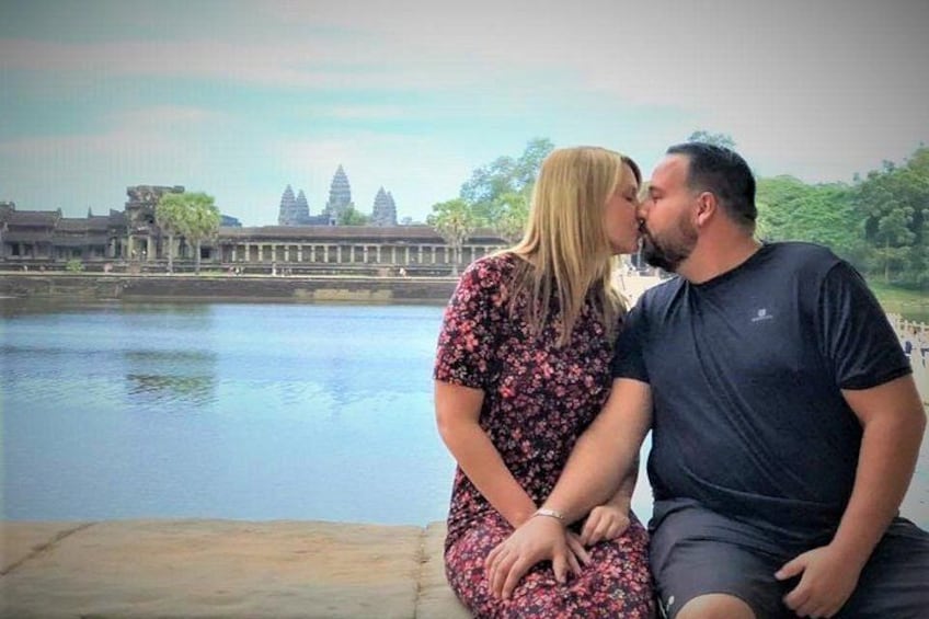 A couple sitting by a body of water with a temple in the background. 1