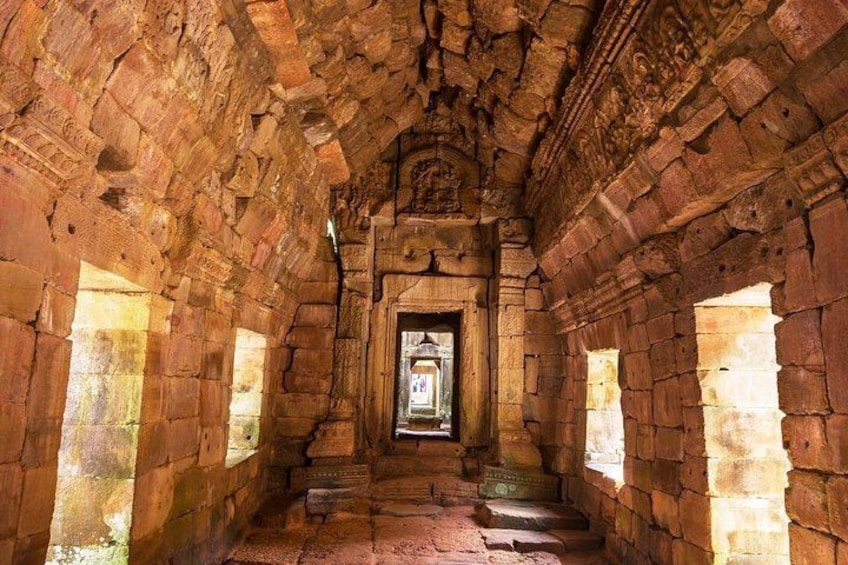 An ancient stone corridor with a central doorway, flanked by two small windows. 3