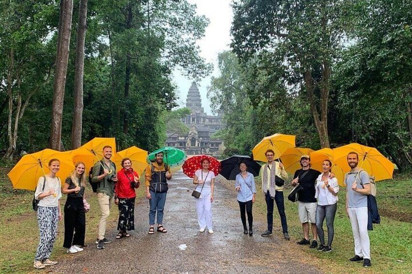 A group of people standing on a path with umbrellas, trees, and a temple in the background. 3