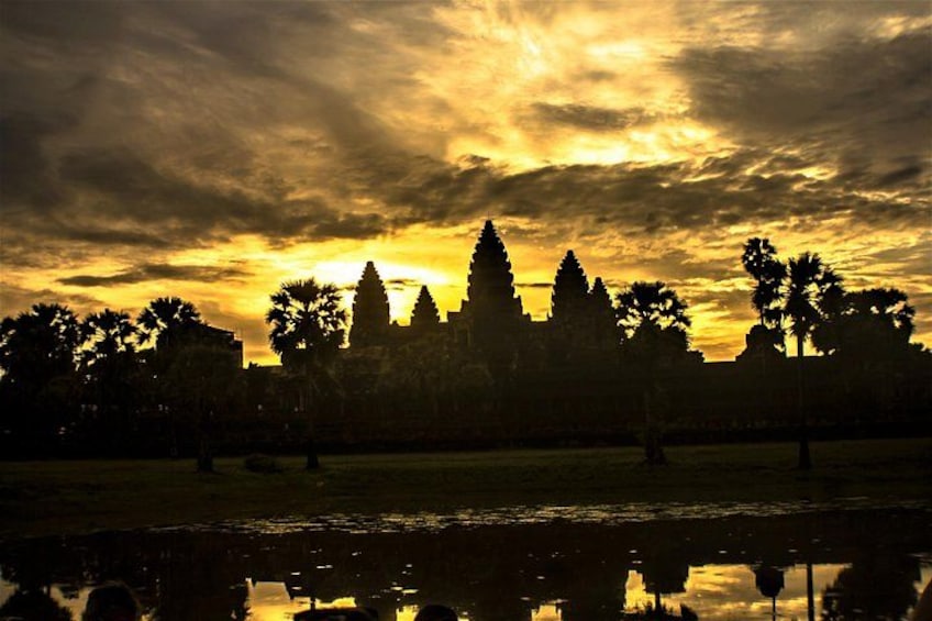 A sunset with a temple silhouette, palm trees, and a calm water body reflecting the sky. 3