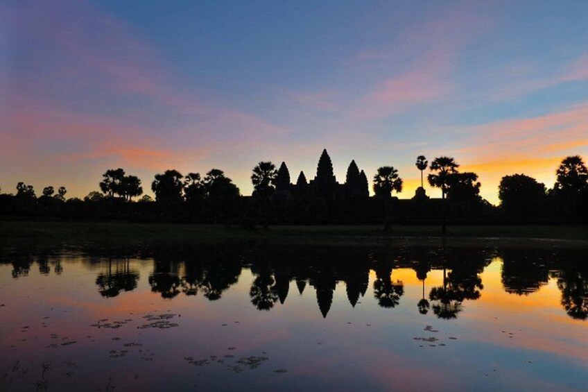 A sunset over a calm lake with reflections of trees and a temple silhouette. 1
