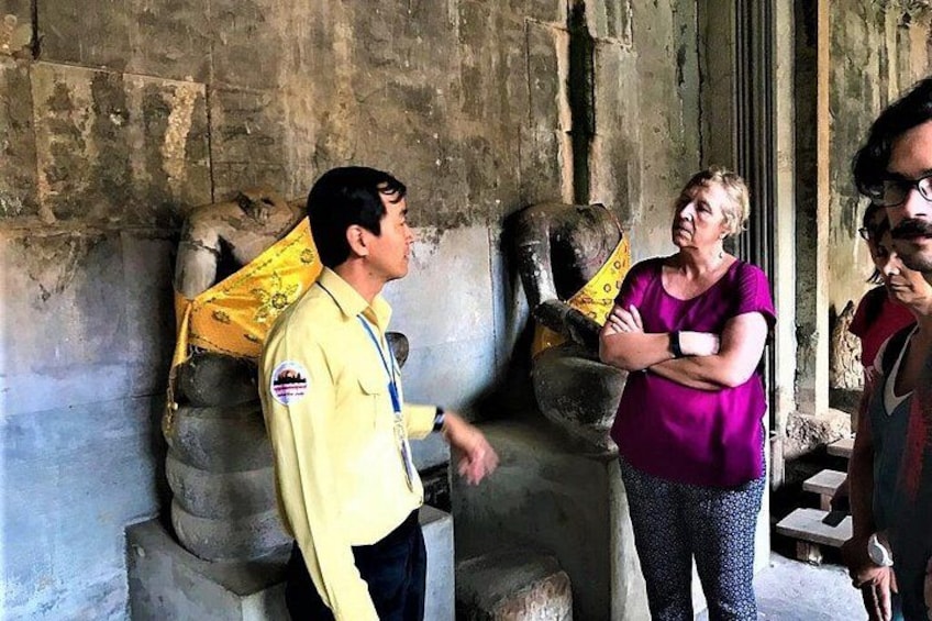 A man in a yellow shirt and a woman in a purple shirt standing in front of a stone structure with a yellow cloth draped over it. 5