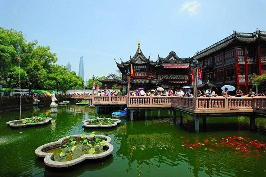 A traditional Chinese pavilion over a pond with lotus plants, surrounded by lush greenery and a modern skyscraper in the background. 1