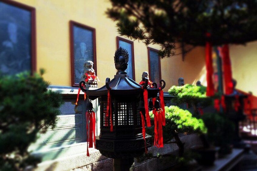 Un farol tradicional con cintas rojas, una estatua y un edificio con ventanas al fondo. 2