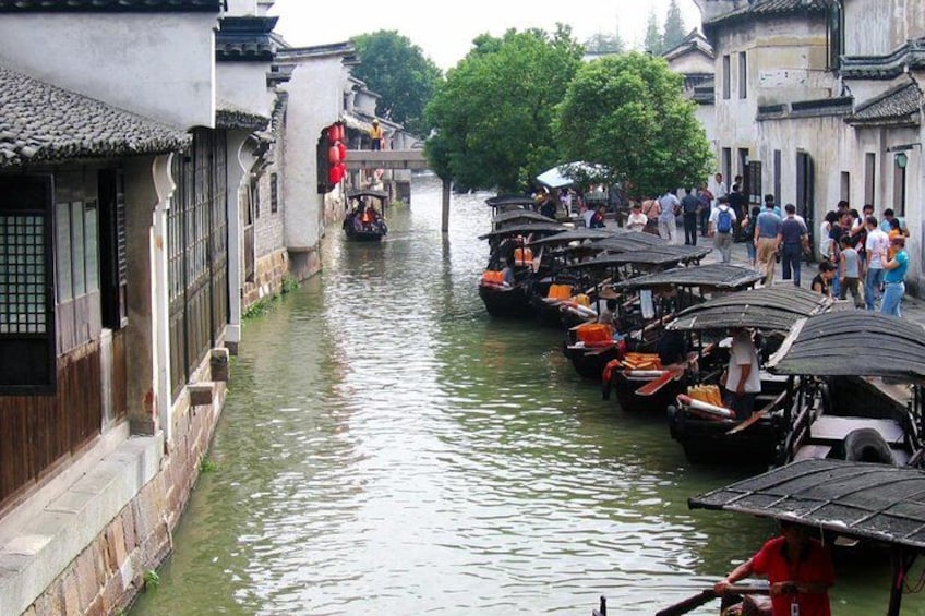 A narrow waterway with traditional buildings on either side, lined with boats and a crowd of people. 2