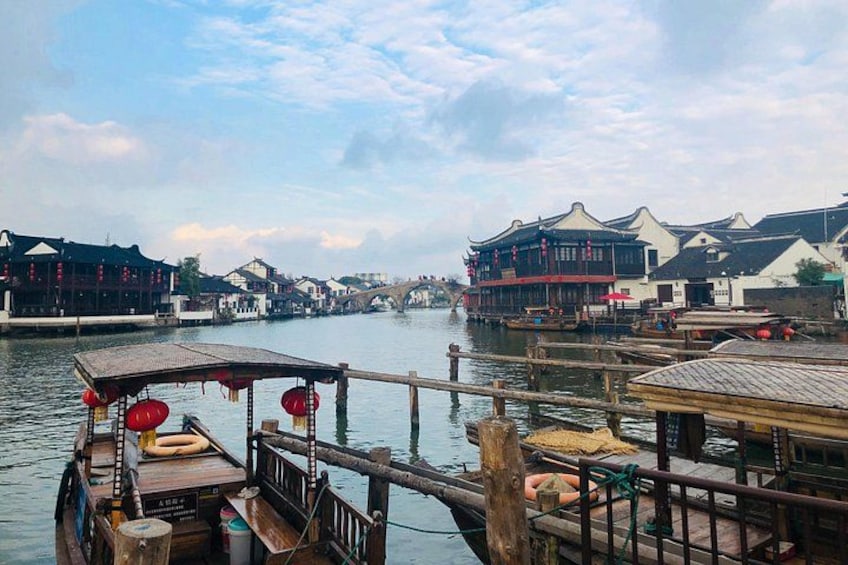 A traditional wooden boat docked at a riverside pier with buildings in the background. 3