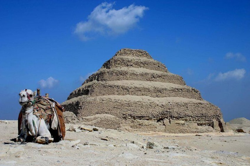 A pyramid structure in a desert with a camel in the foreground. 1