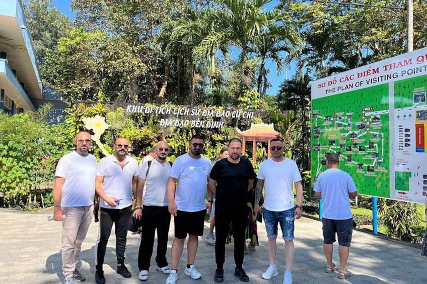 A group of people standing in front of a map and a signboard. 1