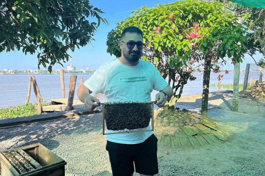A person holding a beehive near a waterfront with trees and a fence in the background. 3