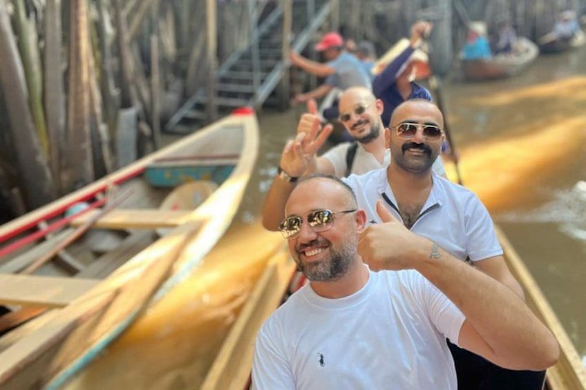People in a boat on a river with wooden boats and a bridge in the background. 4