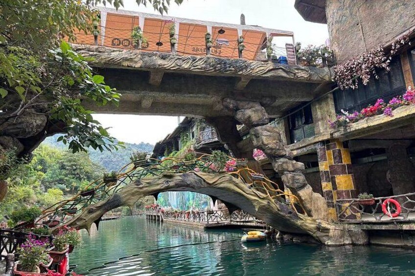 A stone bridge over a river with a tree growing through it, surrounded by greenery and buildings. 4