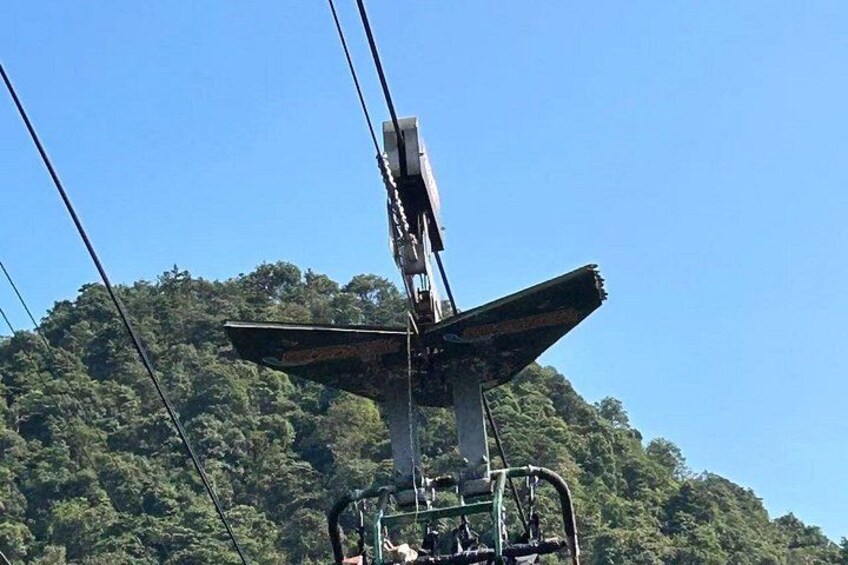 A cable car system with a cable car suspended between two towers, set against a backdrop of a forested hill. 3