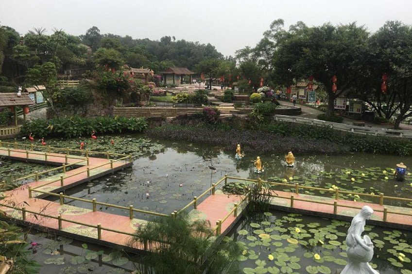 A pond with lily pads, a statue, and a bridge. 1