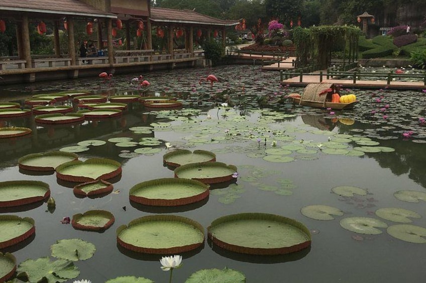 A pond with lily pads, a small boat, and a pavilion with red lanterns. 2