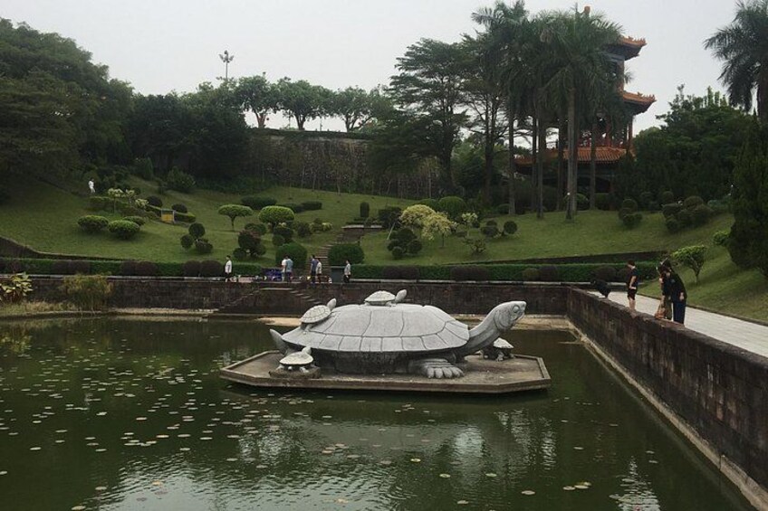 A turtle statue on a platform in a pond, surrounded by a park with trees and a pagoda in the background. 5