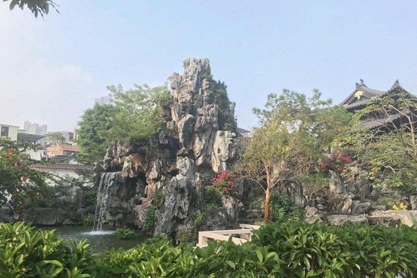 A rocky waterfall, lush greenery, and traditional architecture. 2