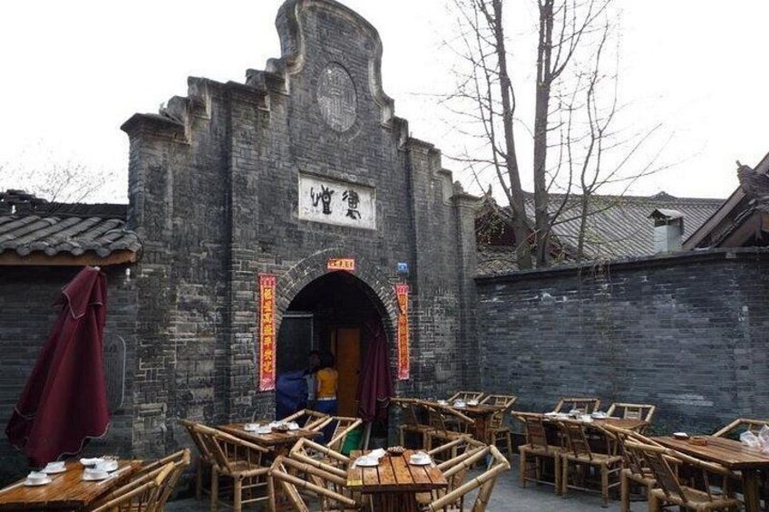 Ein traditionelles chinesisches Gebäude mit einem steinernen Torbogen, Holztischen und Stühlen im Freien. 1