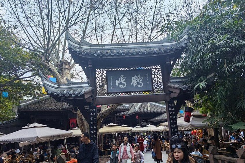 Ein traditioneller chinesischer Pavillon mit einem Schild, umgeben von Marktständen und Menschen. 4