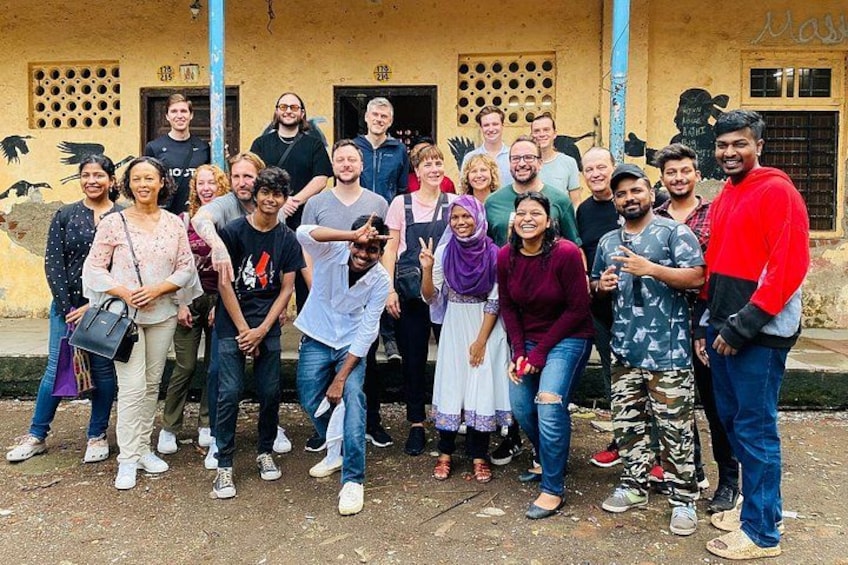 Un grupo de personas posando frente a un edificio con un mural y un poste azul. 4