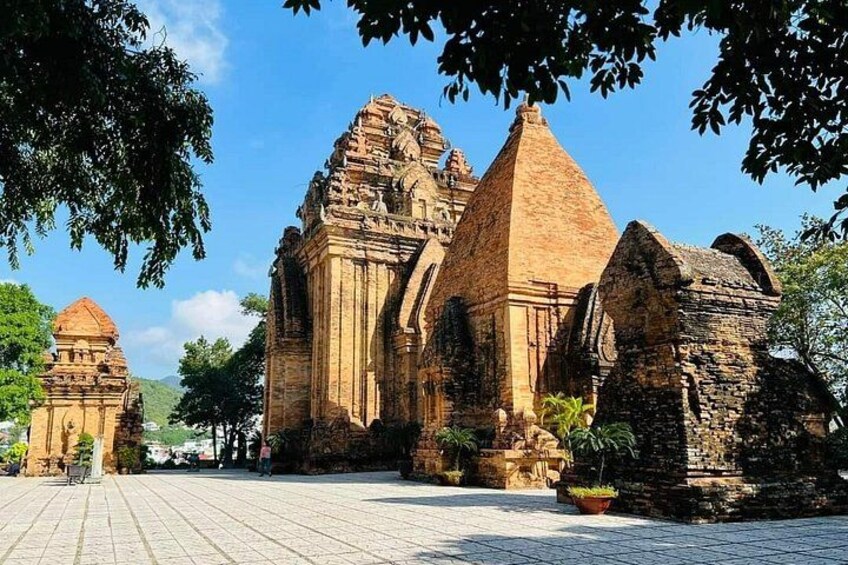 Ancient stone structures with intricate carvings, surrounded by trees and a paved area. 1