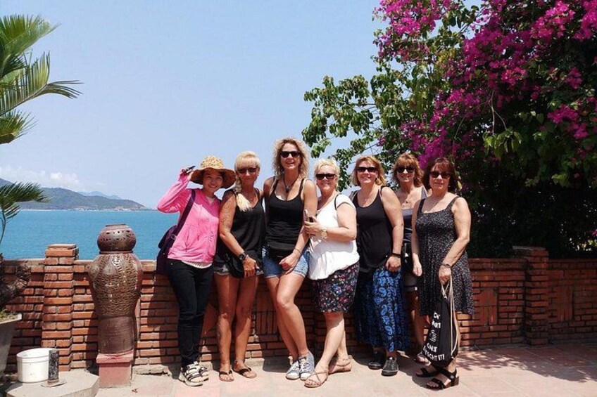A group of people standing by a brick wall with a view of the sea and a pink flowering tree. 3