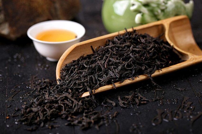 Une louche en bois remplie de feuilles de thé noir, une petite tasse de thé et une pomme verte sur une surface sombre. 4