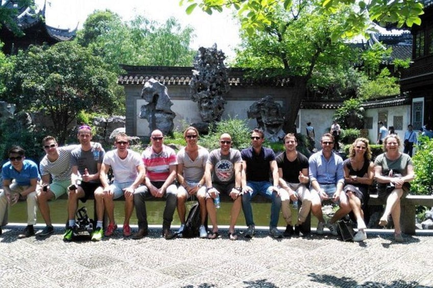 A group of people sitting on a stone bench in a garden with traditional architecture and a stone sculpture in the background. 3