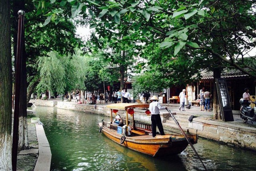A narrow waterway with a wooden boat, people walking along the banks, and trees providing shade. 3
