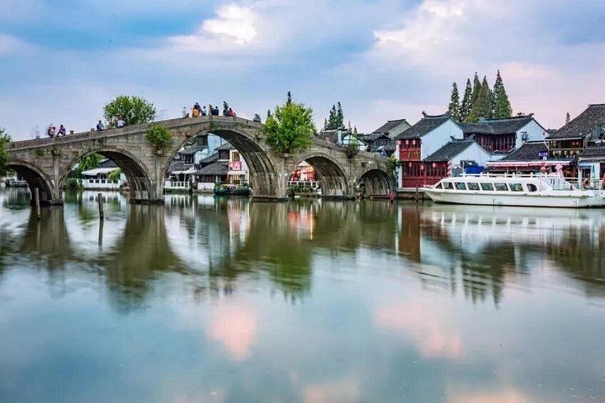 Un puente de piedra sobre un río tranquilo, con edificios tradicionales y un bote a la derecha. 2