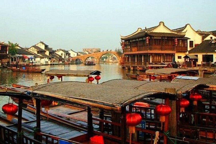 A traditional Chinese water town with wooden buildings, a stone bridge, and boats. 2