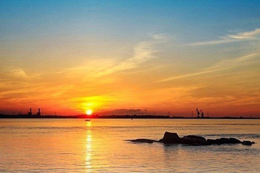 A sunset over a calm body of water with industrial structures in the distance. 2