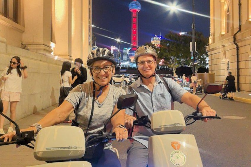 Two people on a tandem bicycle on a city street with a tower in the background. 3