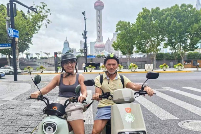 Two people on scooters, a traffic light, and a tower in the background. 1