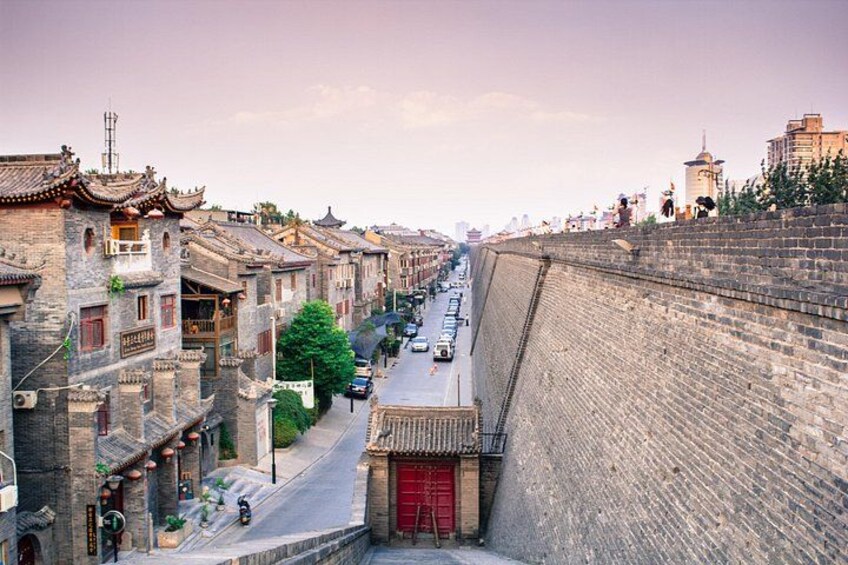 Una calle tradicional con edificios antiguos, un portón rojo y un muro de piedra. 2