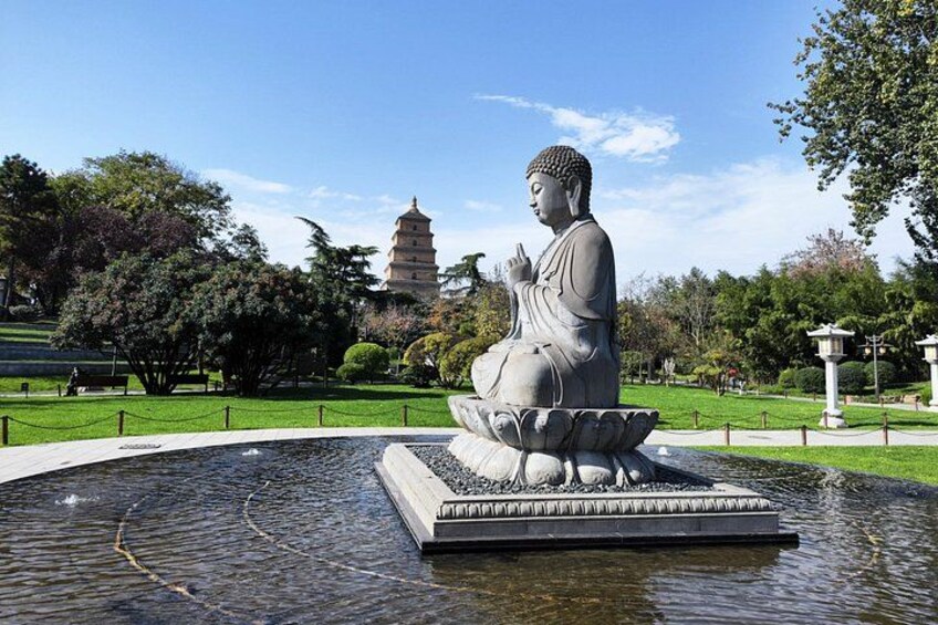 A large Buddha statue sitting on a lotus pedestal in a park with a pagoda in the background. 4
