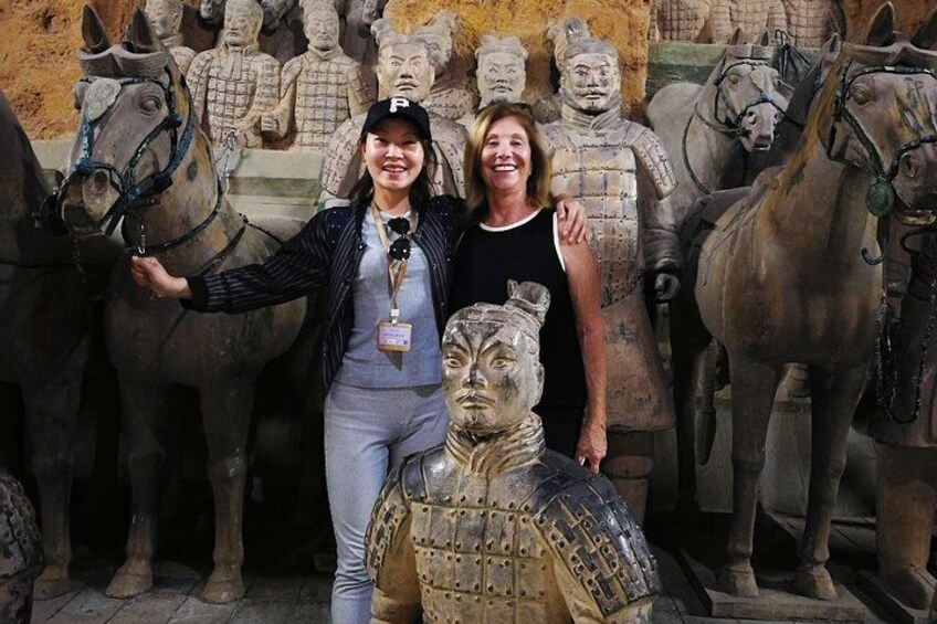 A person standing in front of a row of terracotta horse statues and a large terracotta warrior. 2