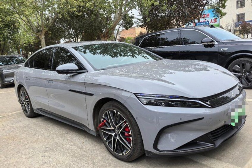 A silver sedan parked in a lot with trees and other vehicles in the background. 3