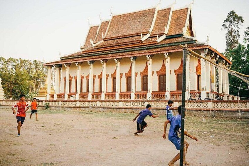 A traditional building with a tiled roof and ornate columns, surrounded by a dirt ground. 1