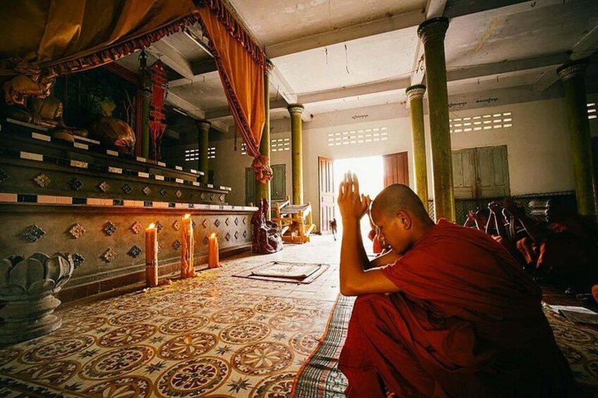 A monk in a red robe praying in a temple with a patterned floor and a canopy. 5
