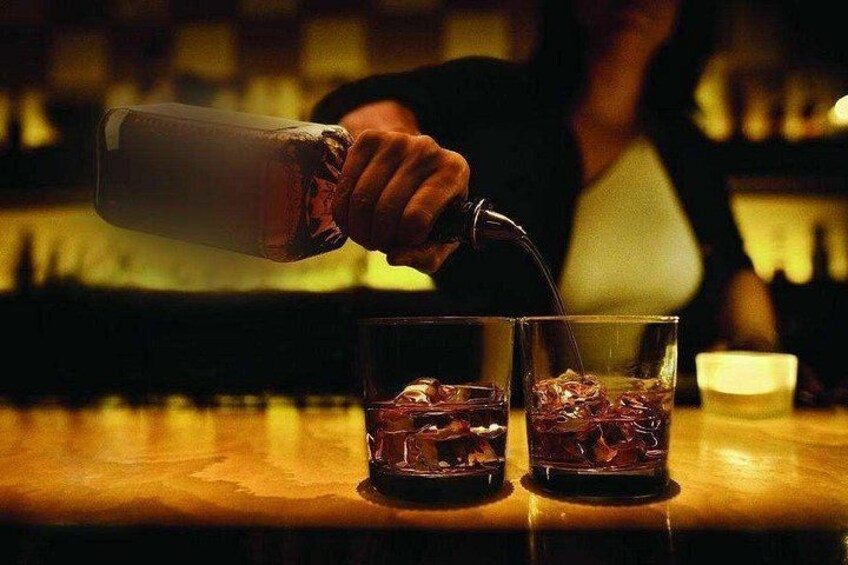 A person pouring a liquid into two glasses on a bar counter. 4