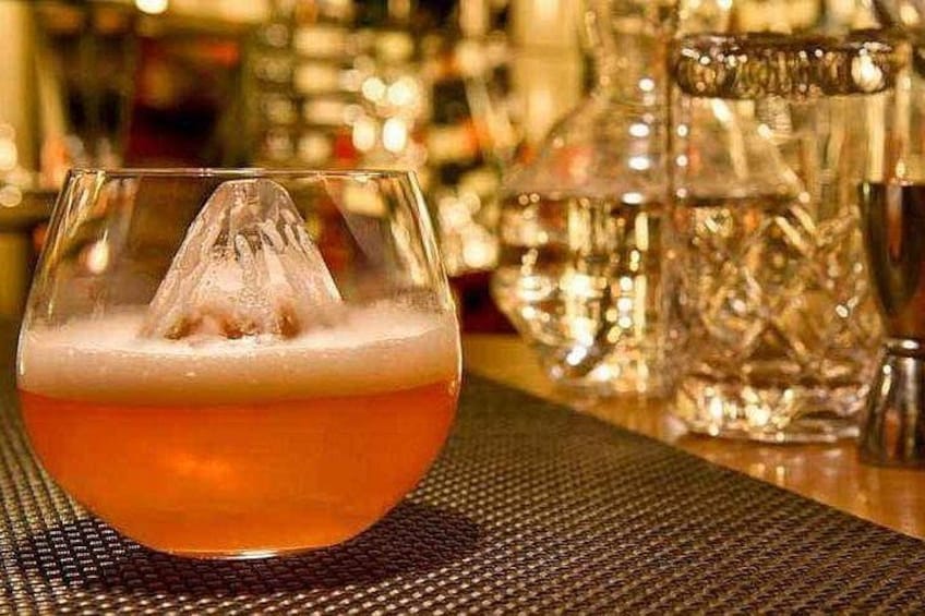 A glass of amber-colored beverage with a frothy head, placed on a textured mat. 3