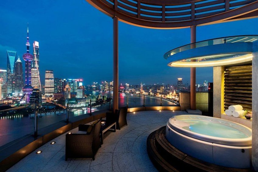 A rooftop terrace with a hot tub, seating area, and a view of the city skyline at dusk. 1