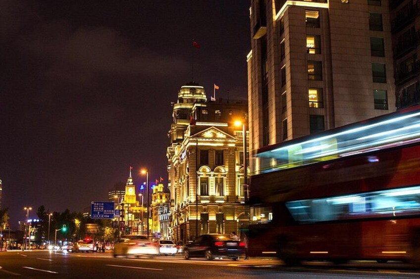 A nighttime cityscape with a brightly lit building, a moving red bus, and a busy street. 4