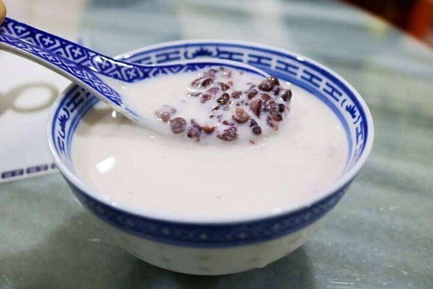 A bowl of white liquid with a spoon, containing small round objects. 4