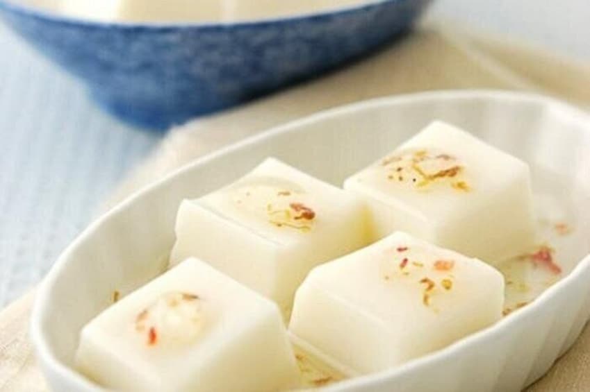 A white dish with four white cubes, possibly cheese or tofu, garnished with red and yellow spices. 5